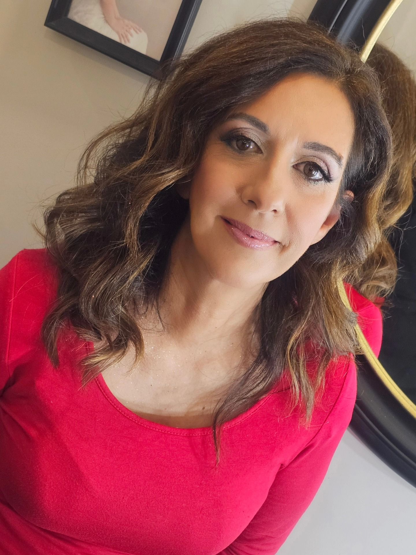 Una donna con i capelli castani ondulati, che indossa un top rosso, sorride alla telecamera.