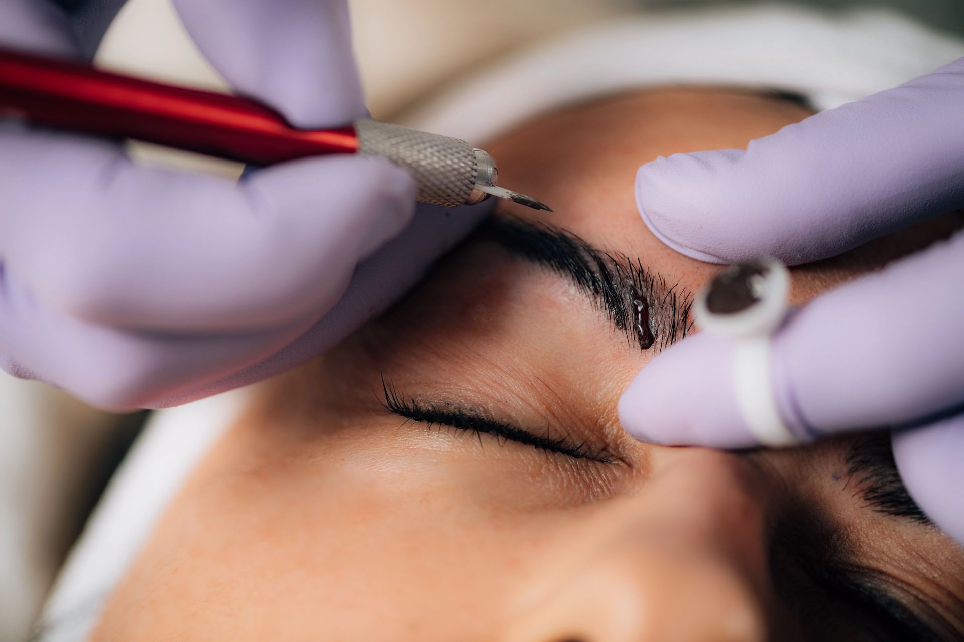 Persona sottoposta a microblading delle sopracciglia; le mani guantate del tecnico utilizzano uno strumento per aggiungere pigmento alle sopracciglia.