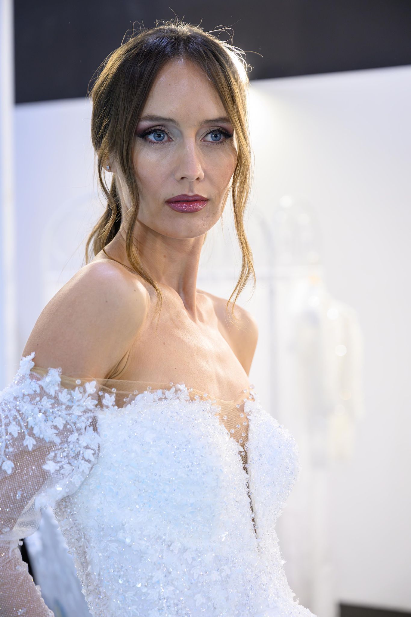 Donna in abito da sposa, che guarda altrove, vicino a un muro bianco.