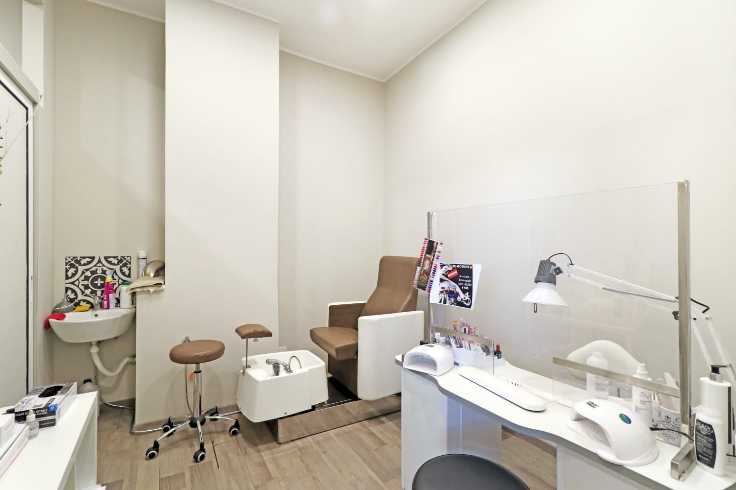 Interno di un salone per unghie con poltrona per pedicure, strumenti e postazione di lavoro. Colori neutri, illuminazione intensa.