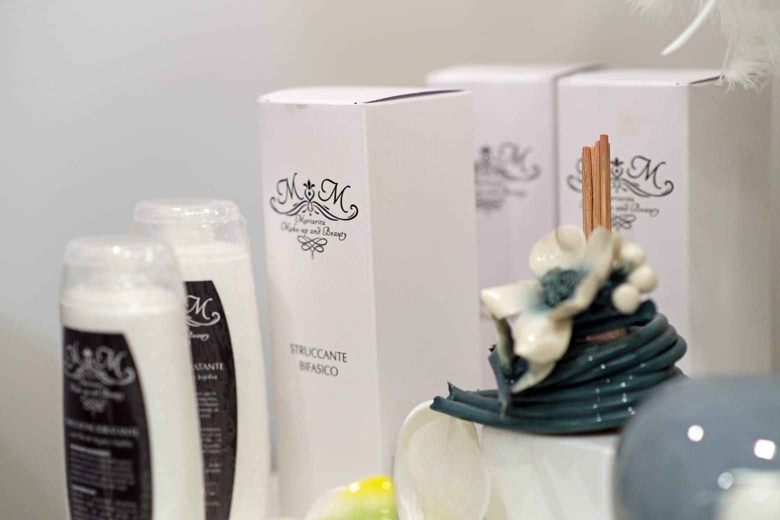 Flaconi e scatole di prodotti bianchi con scritte nere e un ornamento floreale in ceramica.