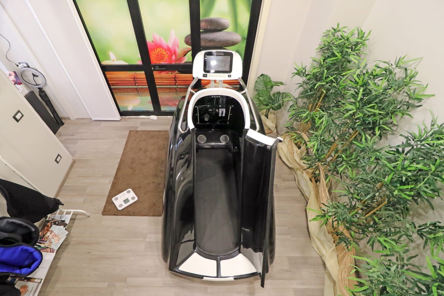 Poltrona massaggiante bianca e nera in un ambiente simile a una spa. Include un paravento, un piccolo tappeto e vegetazione artificiale.