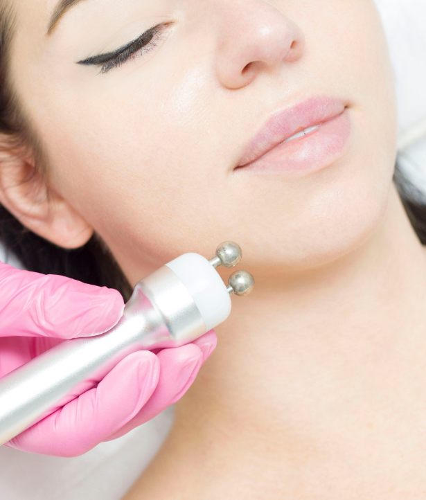 Persona che riceve un trattamento viso con un dispositivo portatile, primo piano. La mano guantata rosa tiene il dispositivo vicino al viso.