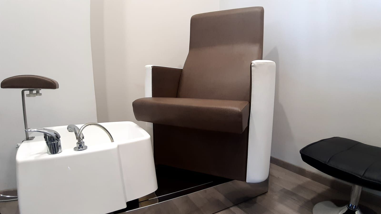 Una postazione per pedicure con una poltrona marrone e un pediluvio bianco in un ambiente da salone.