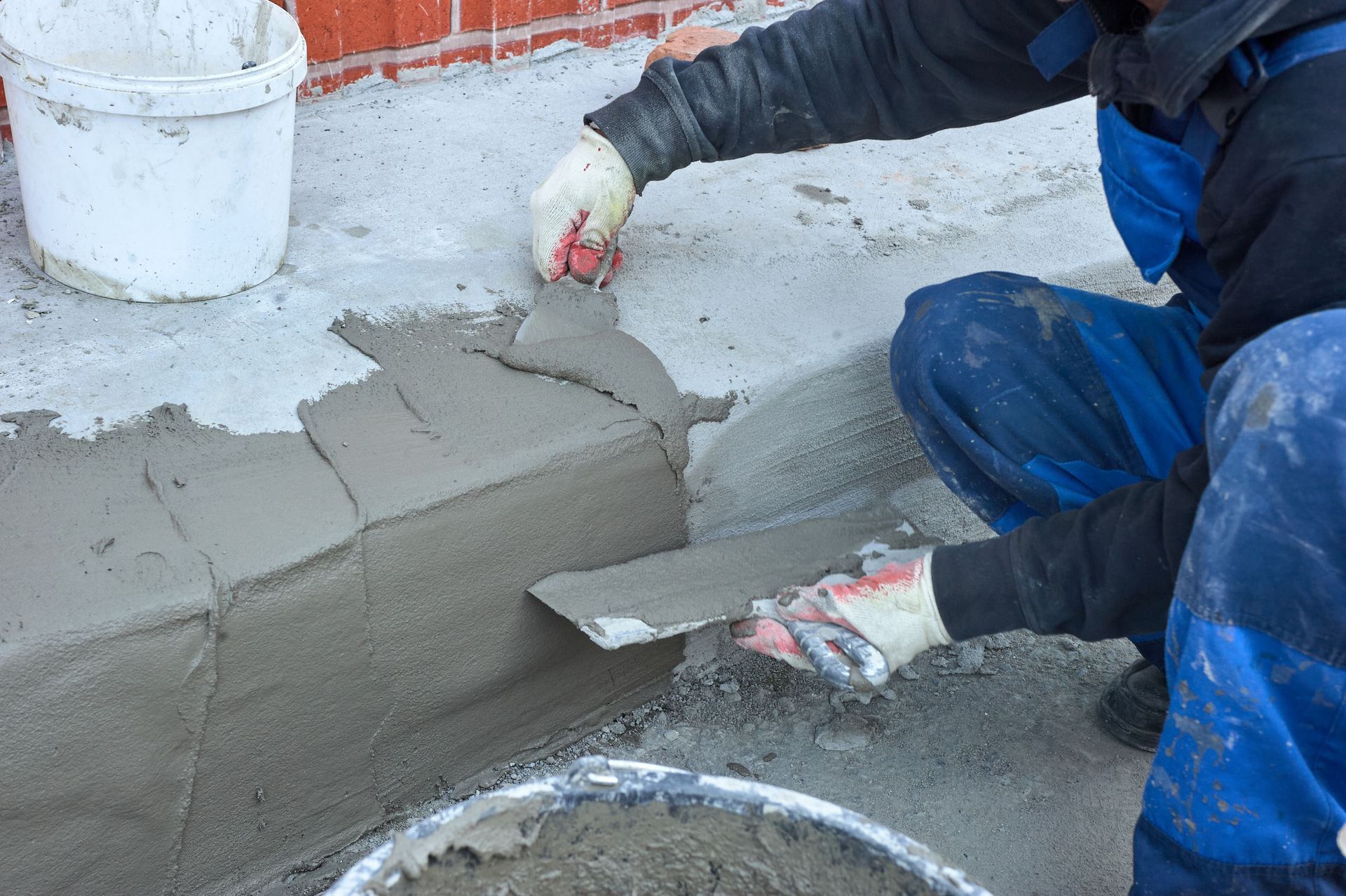 A man is kneeling down and using a trowel to spread concrete on a sidewalk.