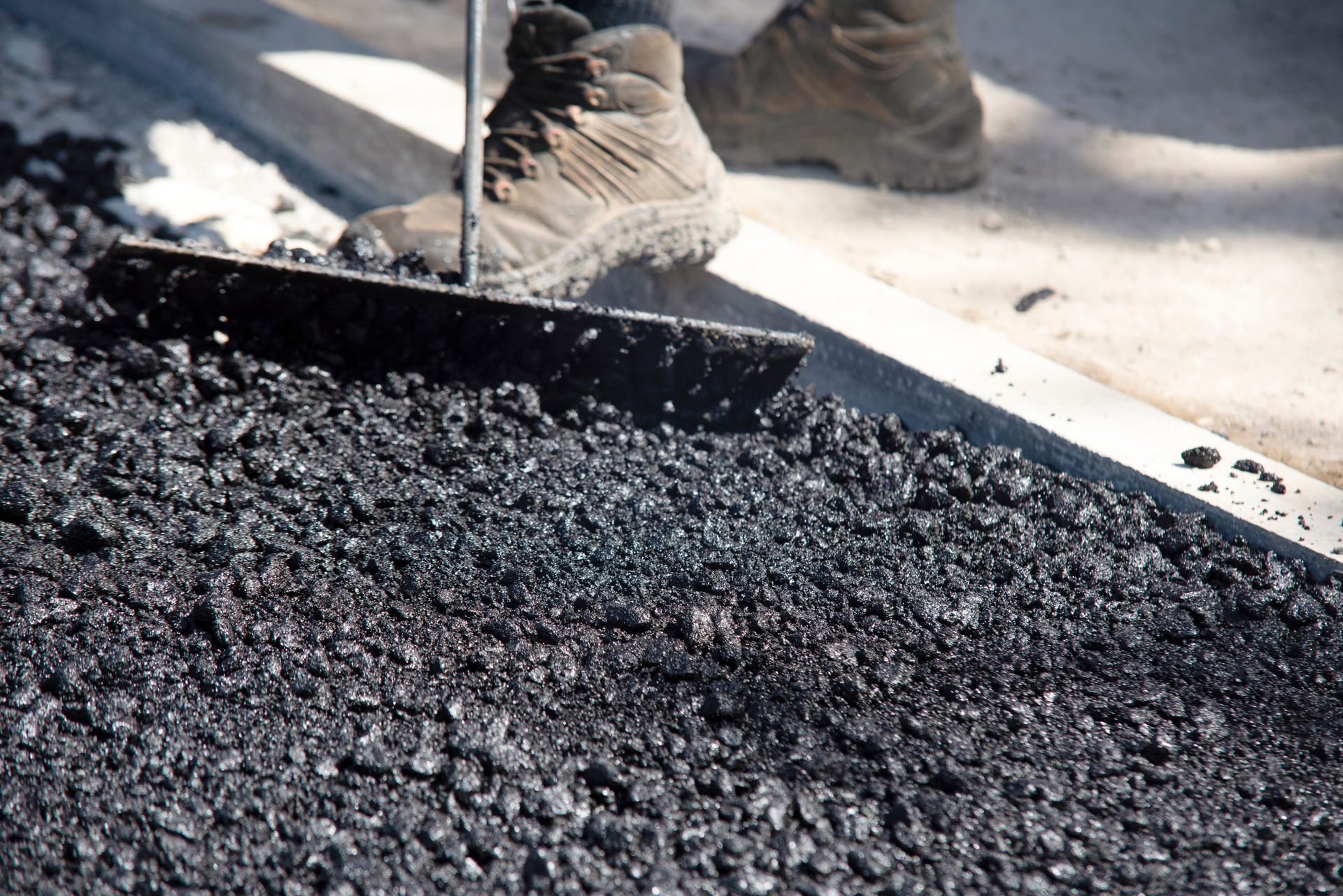 A person is raking a pile of asphalt with a shovel.