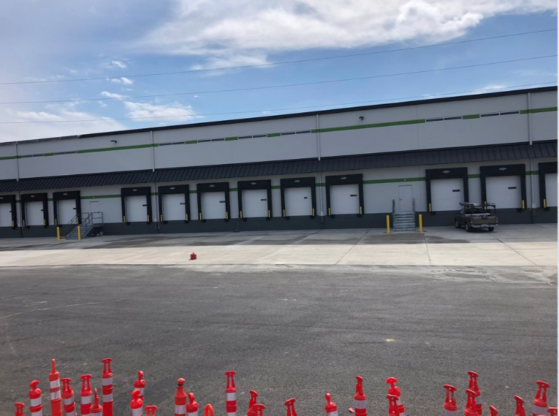 A warehouse with a lot of loading doors and a lot of red cones in front of it.