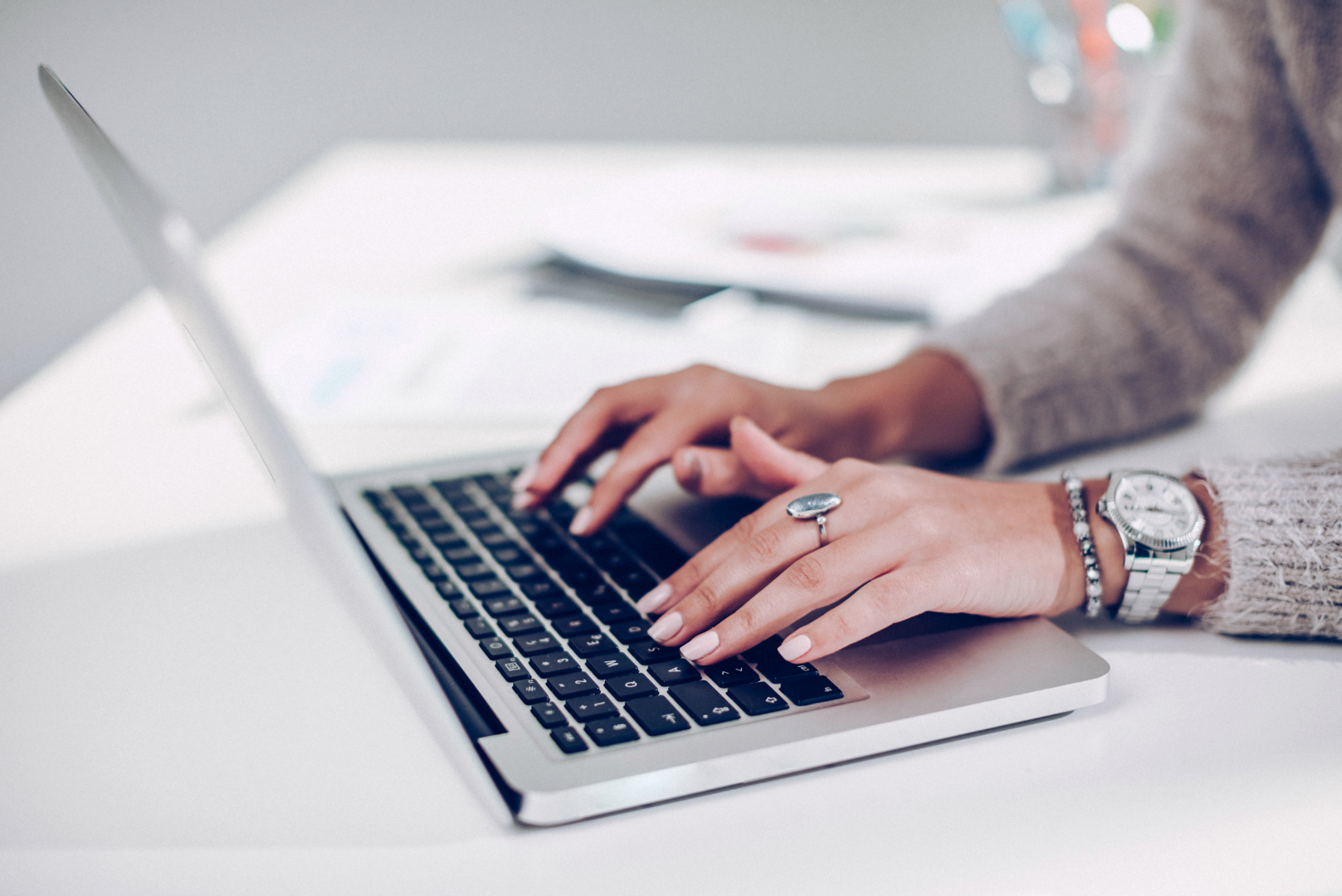 A woman is typing on a laptop computer while wearing a watch.