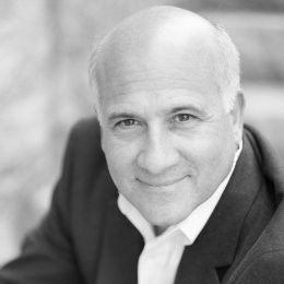 A man in a suit and white shirt is smiling in a black and white photo.