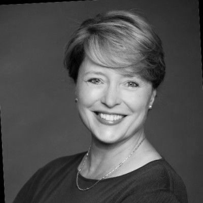 A woman wearing glasses and a white jacket is smiling in a black and white photo.