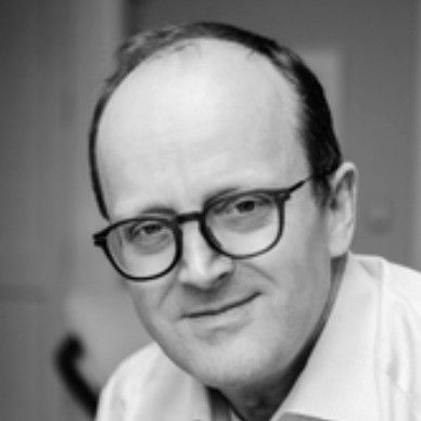 A man in a suit and white shirt is smiling in a black and white photo.