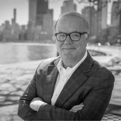 A woman wearing glasses and a white jacket is smiling in a black and white photo.