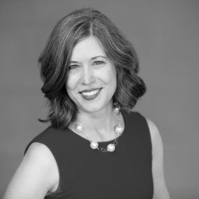 A man in a suit and glasses is smiling in a black and white photo.
