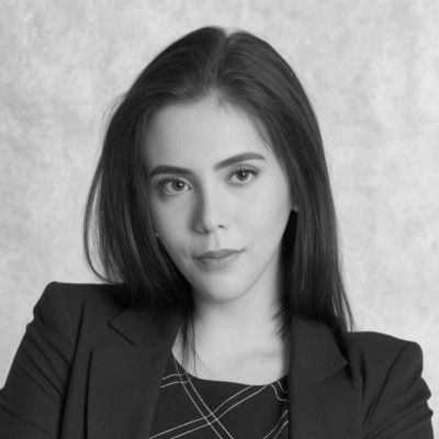 A woman in a black dress and pearl necklace is smiling in a black and white photo.