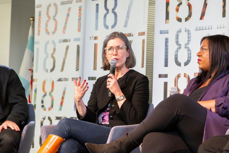 A woman is speaking into a microphone while sitting in front of a wall with numbers on it.