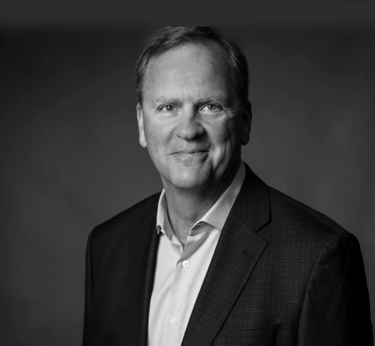 A man in a suit and white shirt is smiling in a black and white photo.