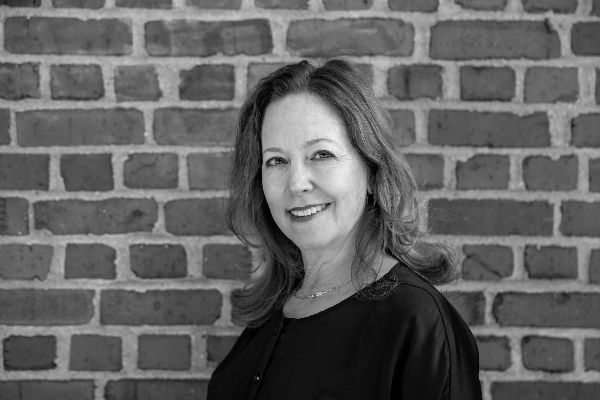 A woman is smiling in front of a brick wall in a black and white photo.