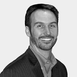 A man with a beard is smiling in a black and white photo.