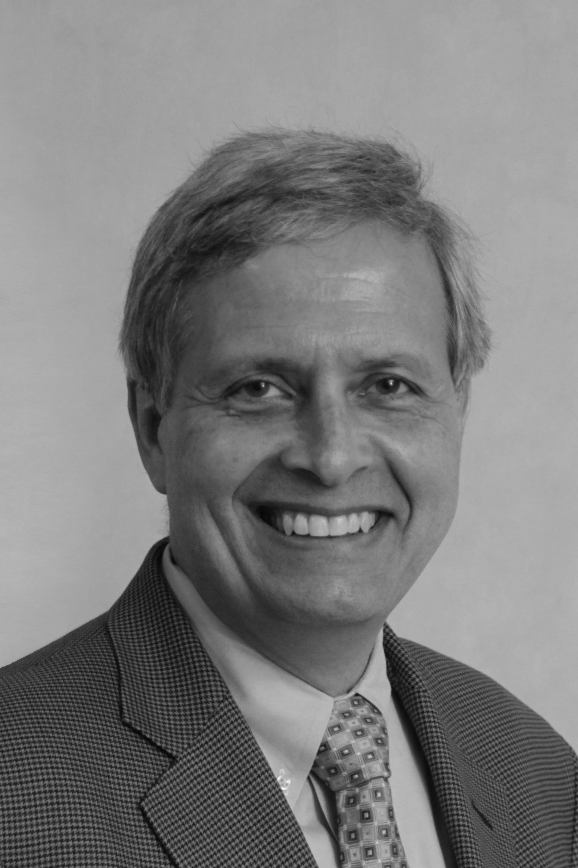 A man in a suit and tie is smiling in a black and white photo.