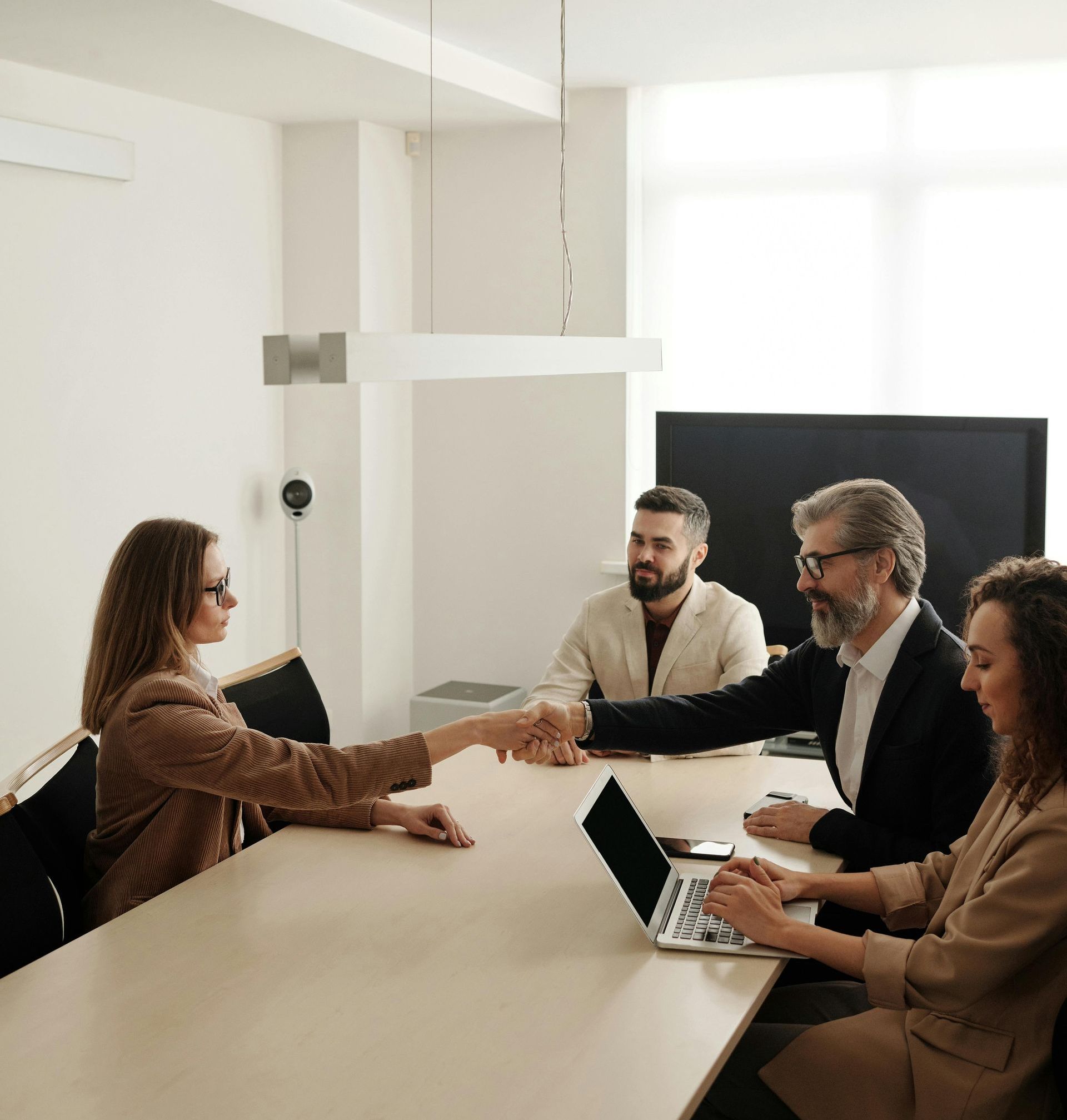 A group of people are sitting around a table shaking hands.