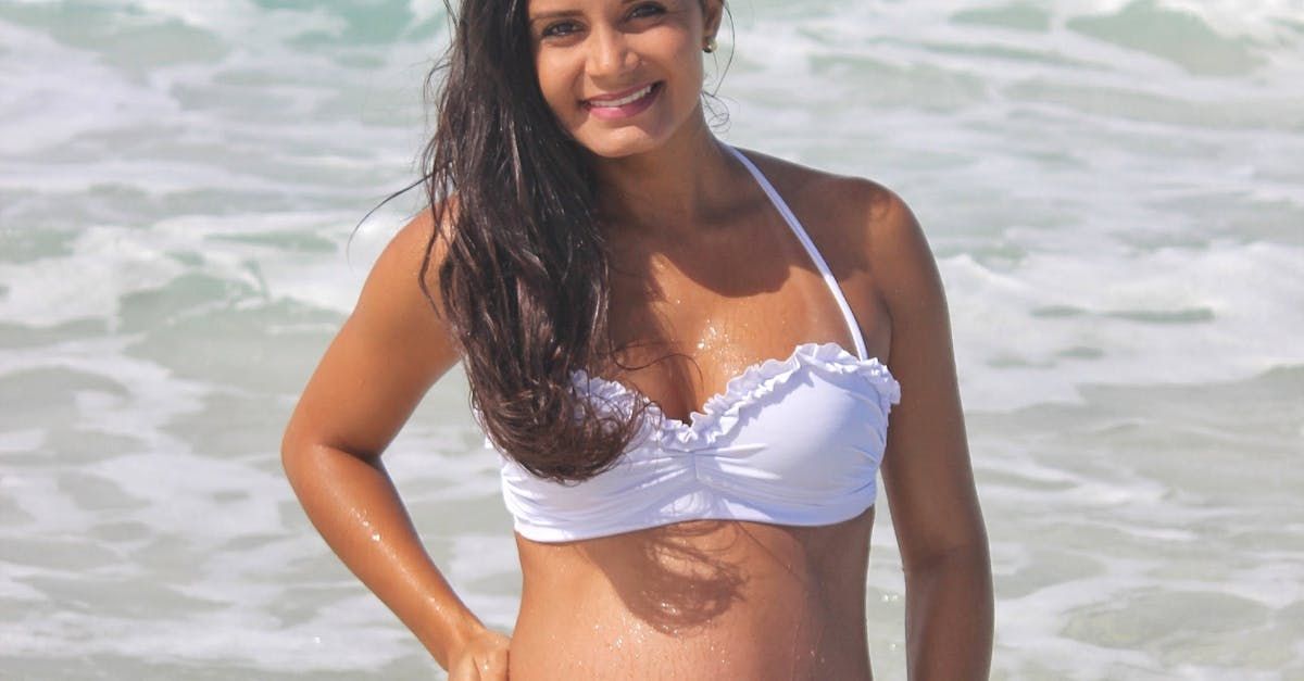 A pregnant woman in a white bikini is standing in the ocean.