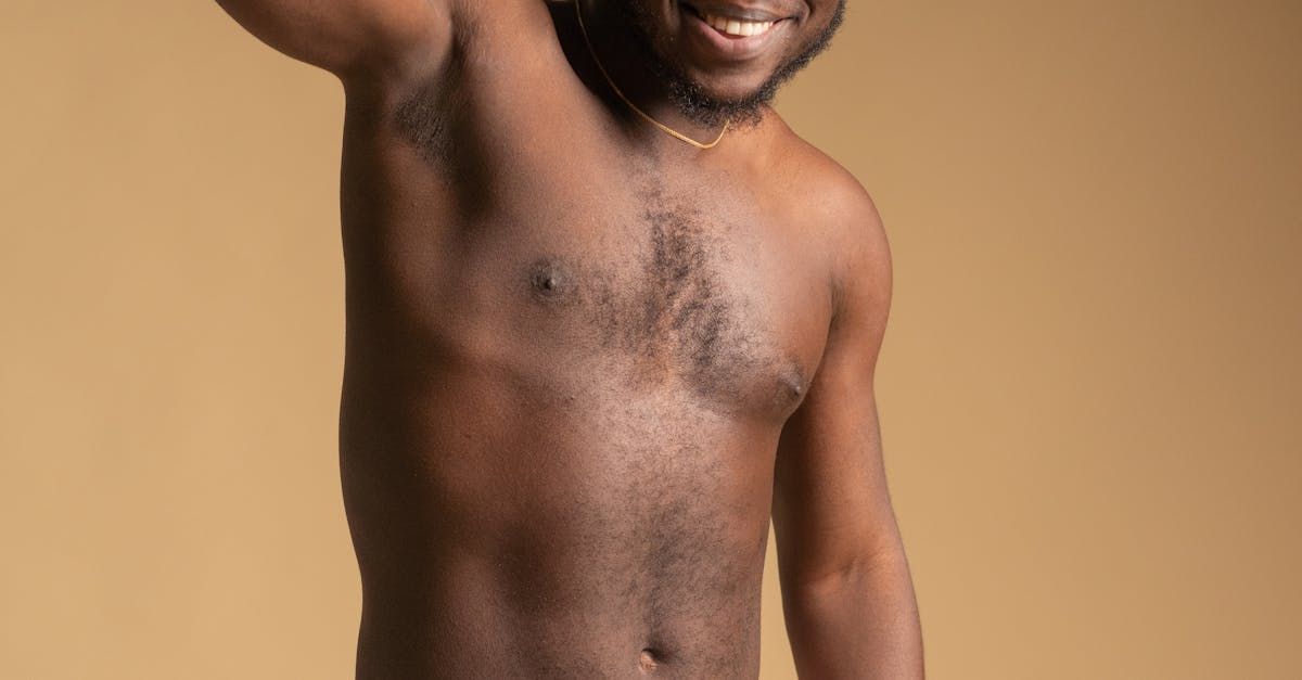 A shirtless man is standing in front of a brown background.