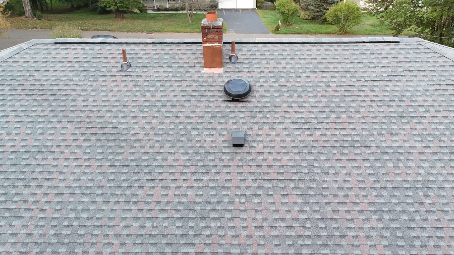 Overhead view of a house roof with grey shingles, a chimney, and vents.