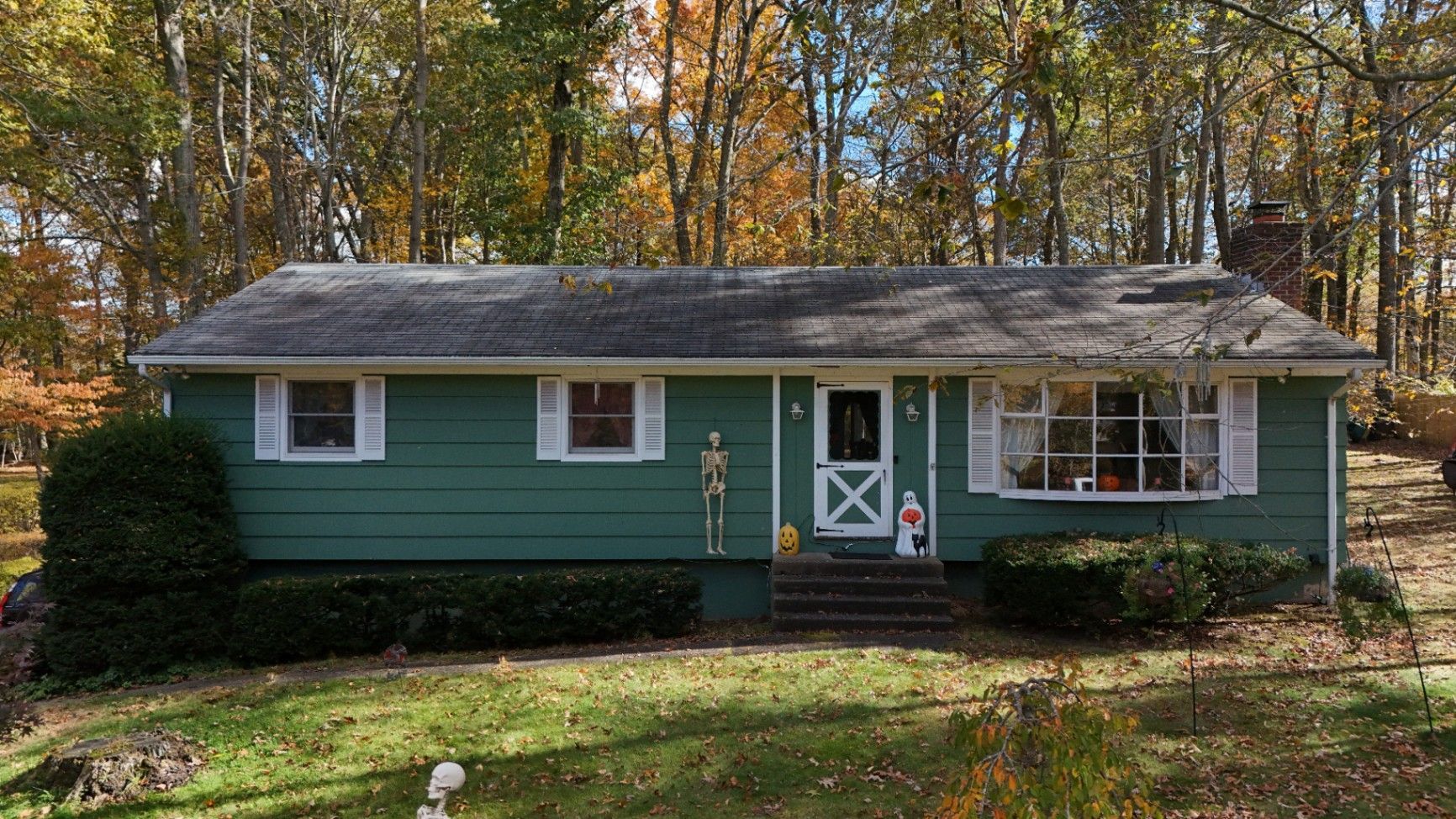 Green ranch house with white trim, set in a yard with fall foliage.