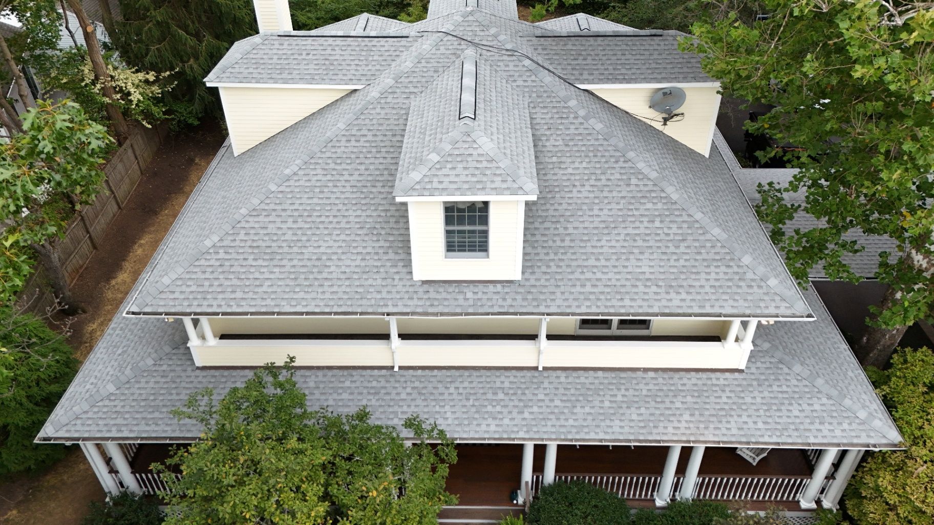 Overhead view of a house with a gray roof, white porch, and surrounding trees.