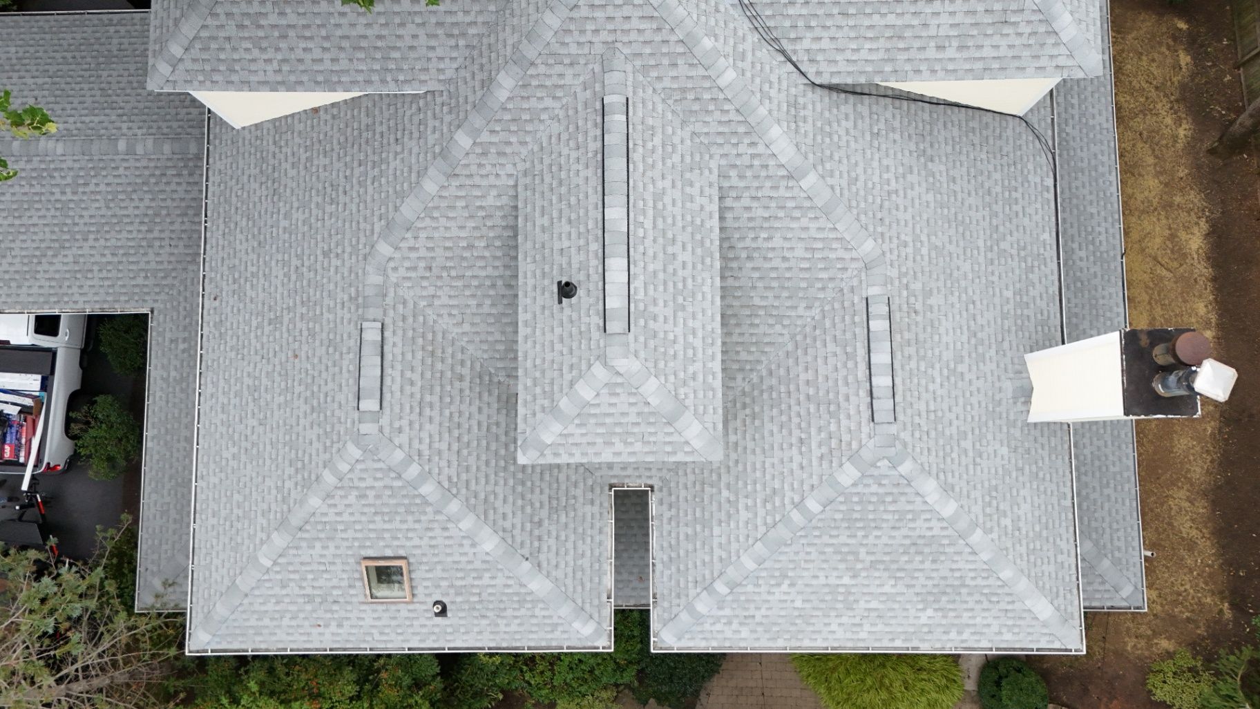 Overhead view of a house with a gray shingled roof, trees, and a white truck.