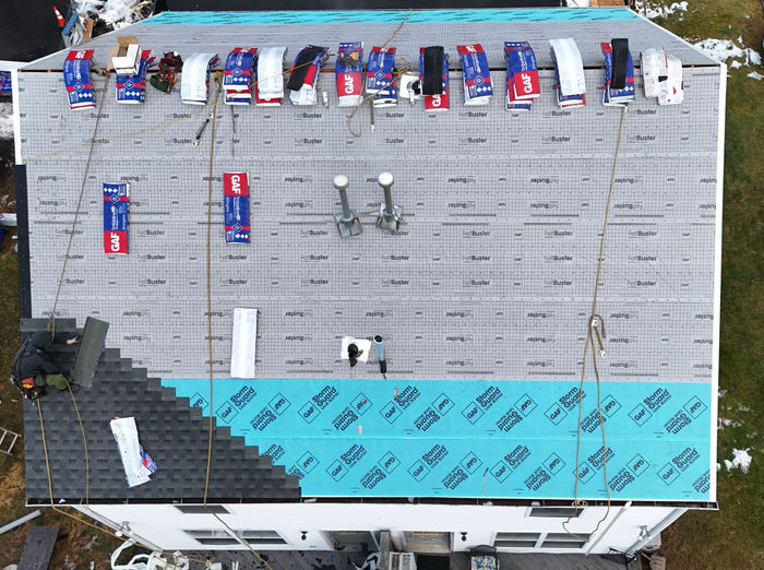 Overhead view of a house roof partially covered with shingles, blue underlayment, and materials.