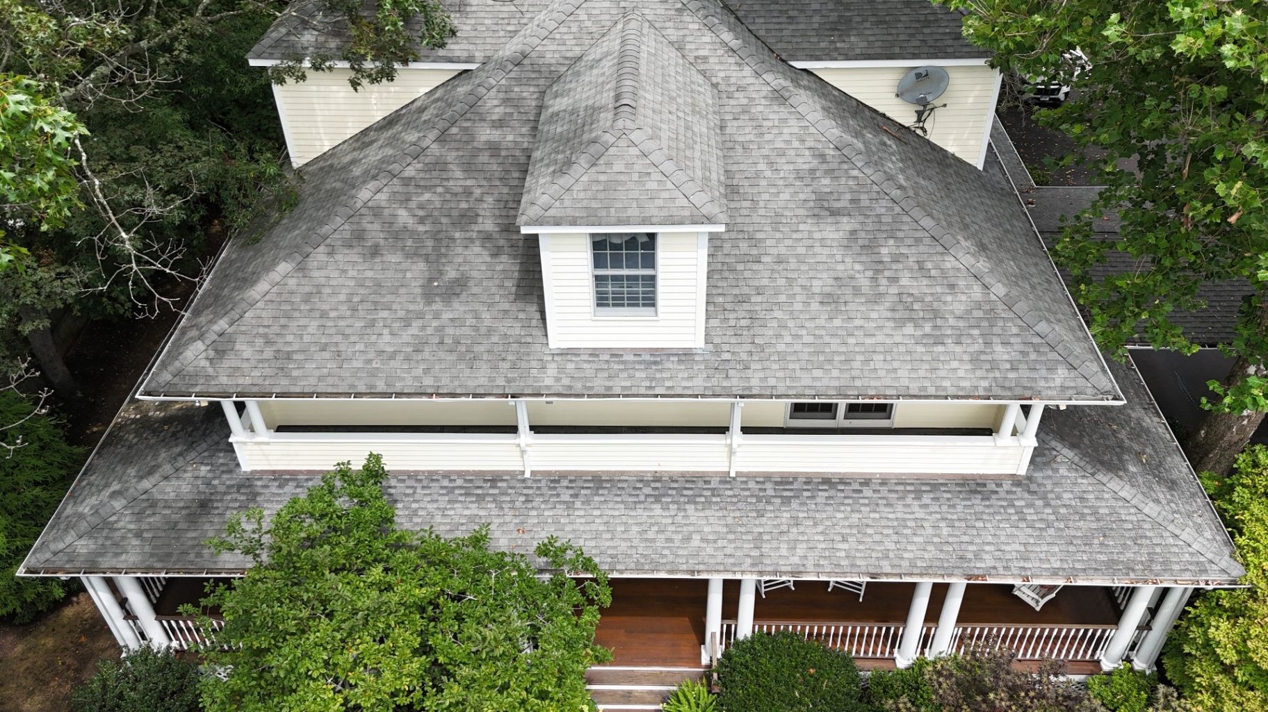 Overhead view of a gray-roofed house with a porch, a dormer, and surrounded by trees.