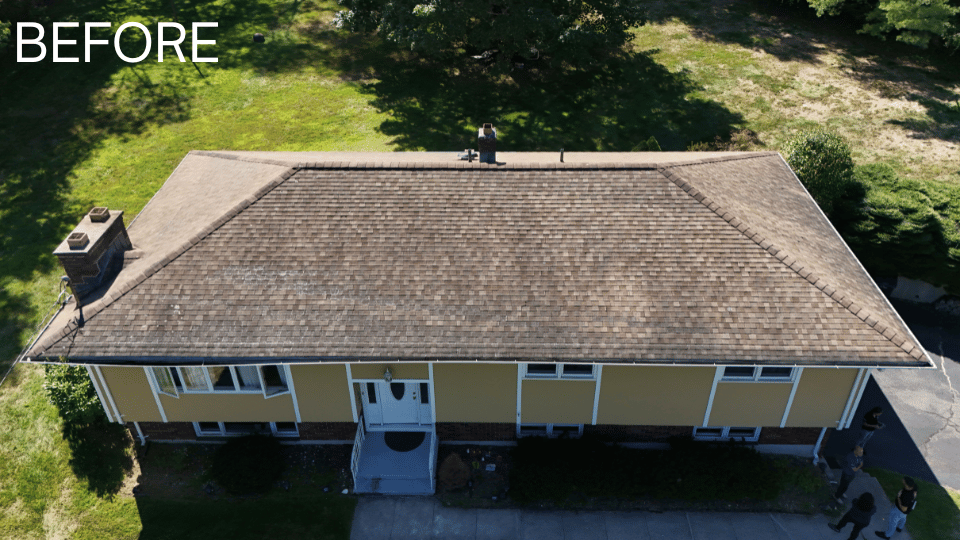 Overhead view of a yellow house with a brown roof and chimney, surrounded by green trees and grass.