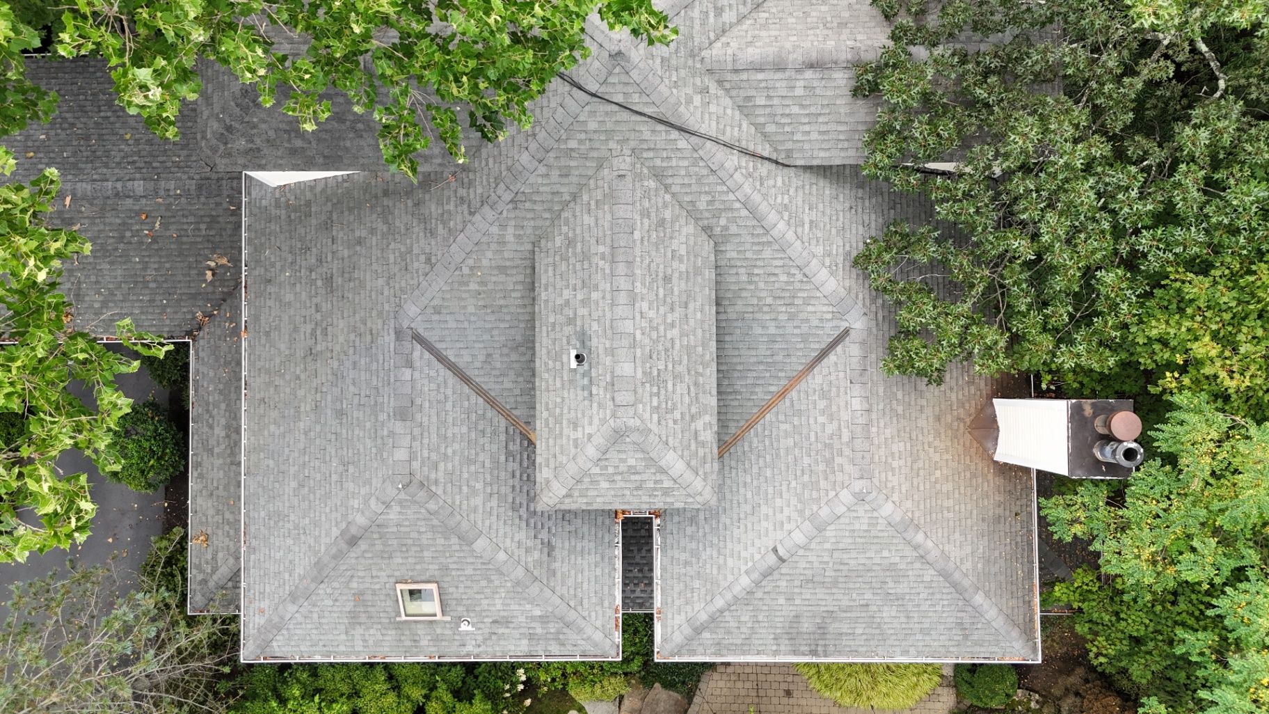 Overhead view of a house with a gray shingle roof, surrounded by green trees.