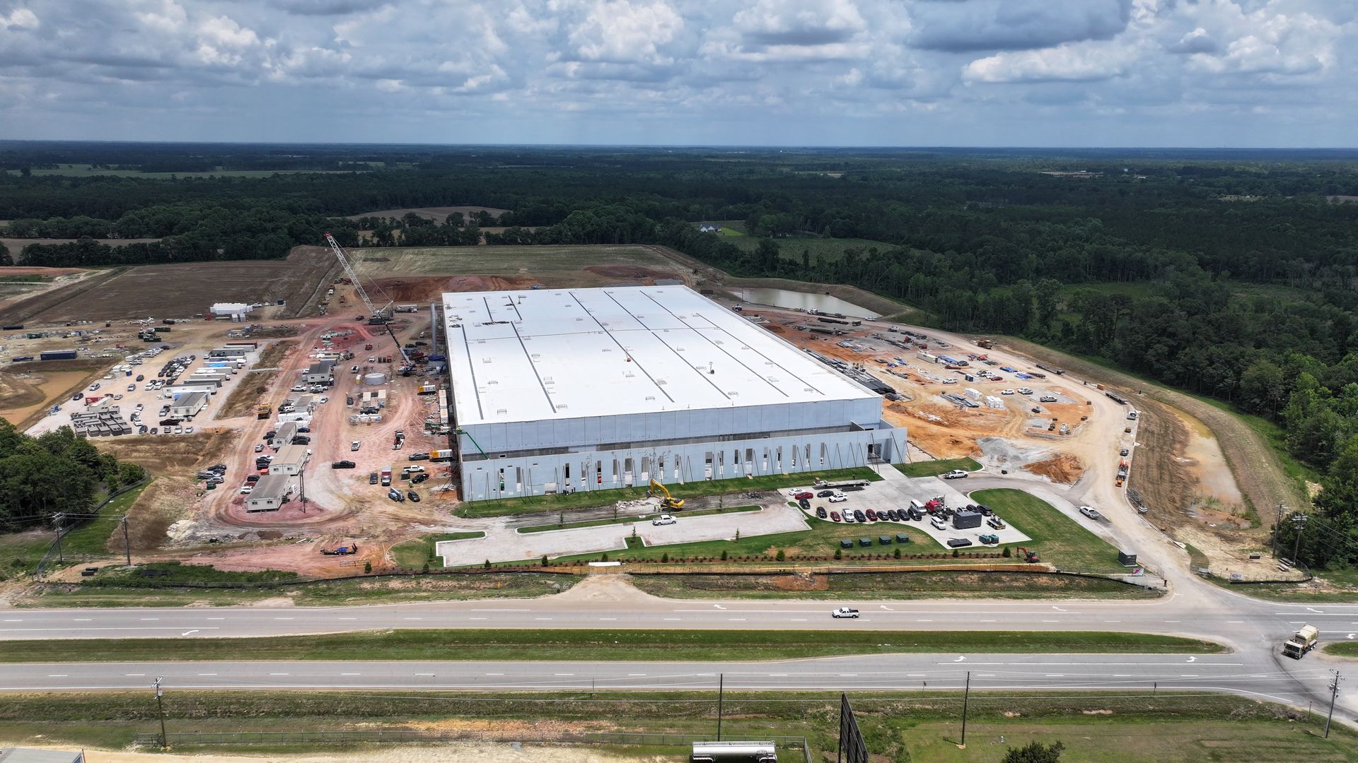 An aerial view of a large building under construction surrounded by trees and a road.