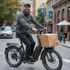 Un homme sur un vélo électrique sourit et livre un colis. Rue de la ville en arrière-plan.