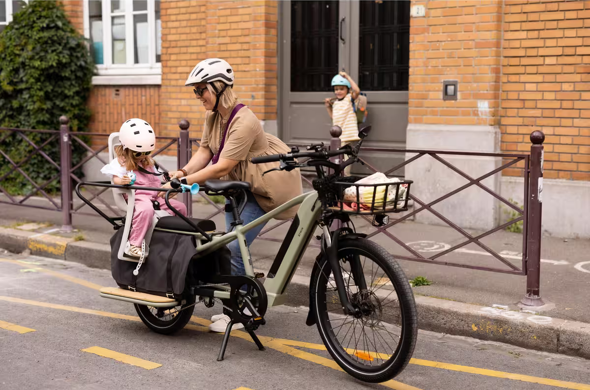 Rangée de vélos cargo électriques noirs garés sur un trottoir devant un bâtiment avec des vitrines.