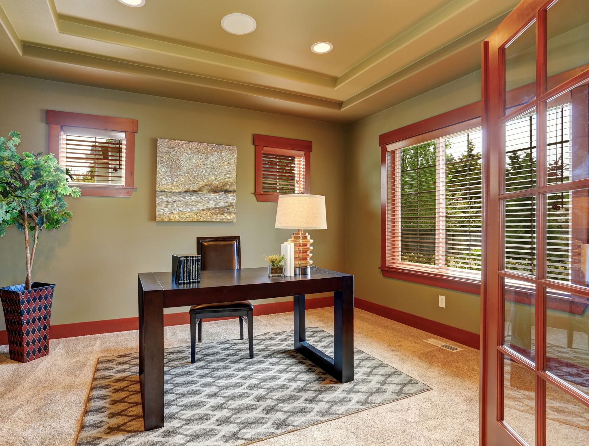 A home office with a desk , chair , lamp and large windows.