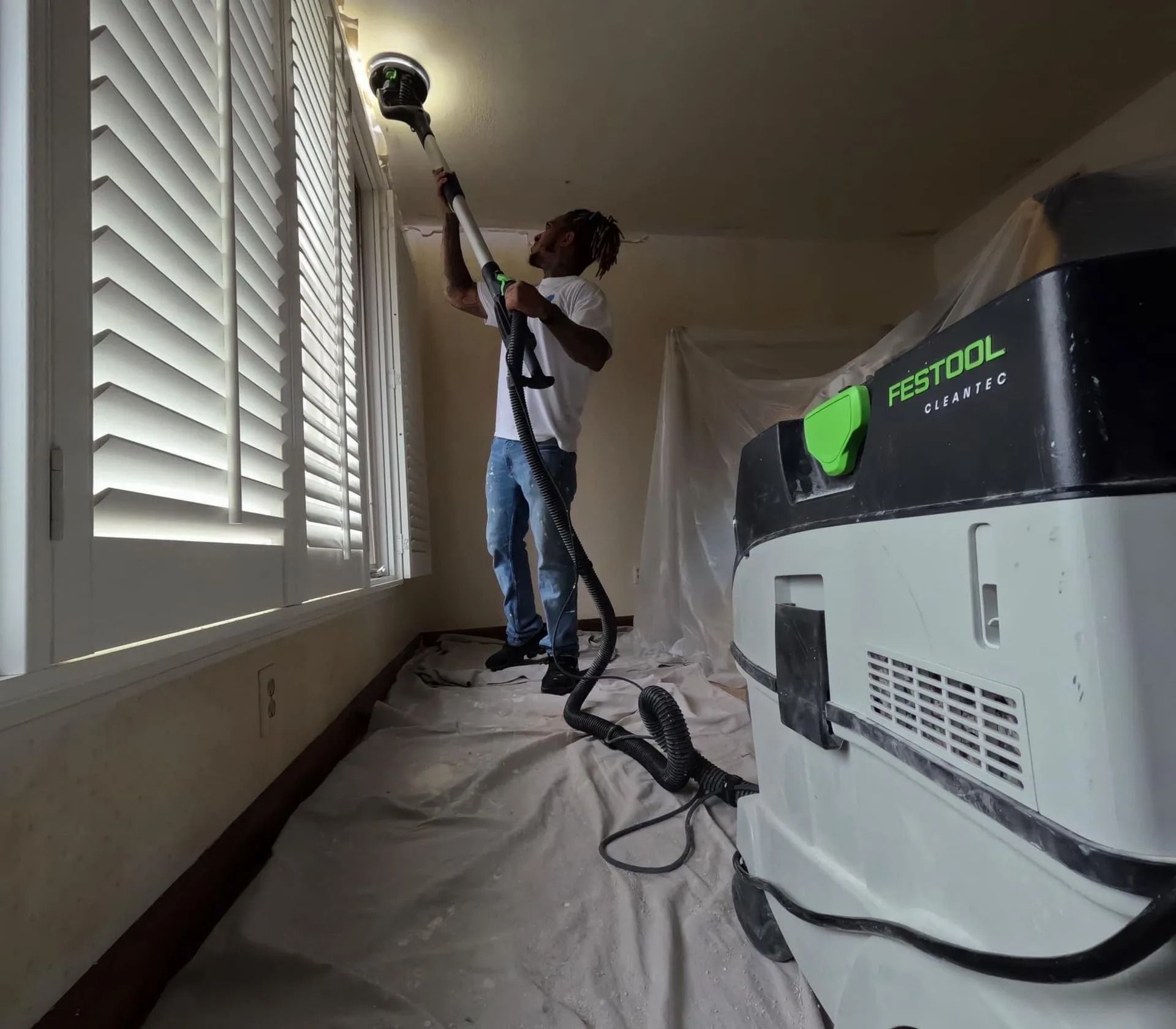 A man is using a festool vacuum cleaner to clean a ceiling
