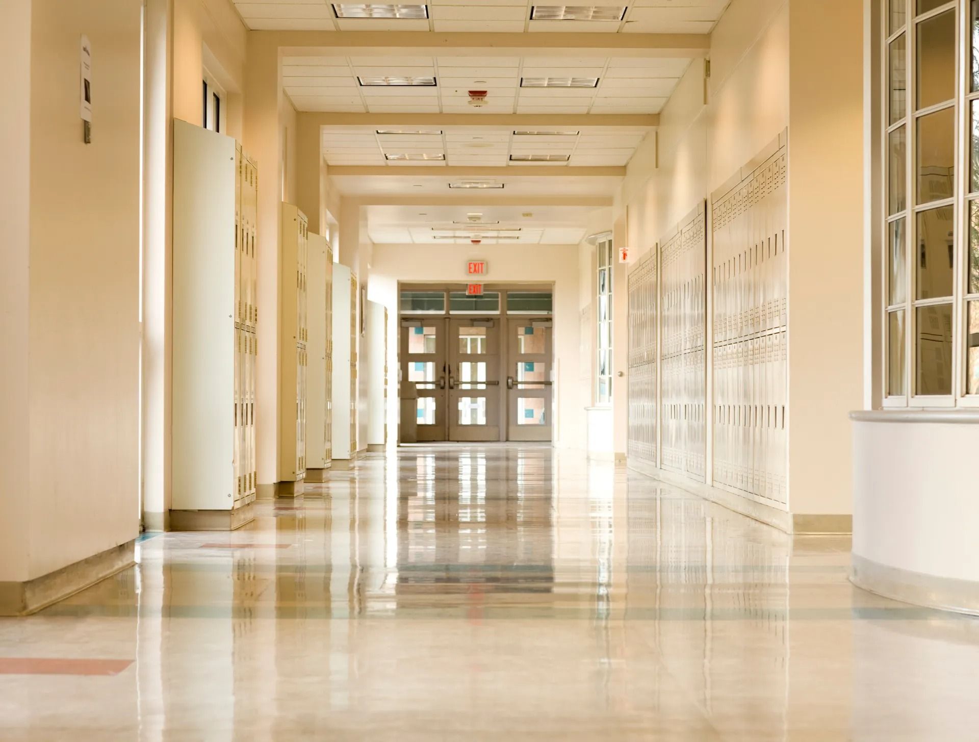 An empty school hallway with lockers and a red exit sign