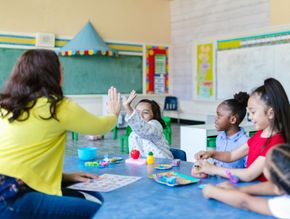 A teacher is giving a high five to a group of children in a classroom.