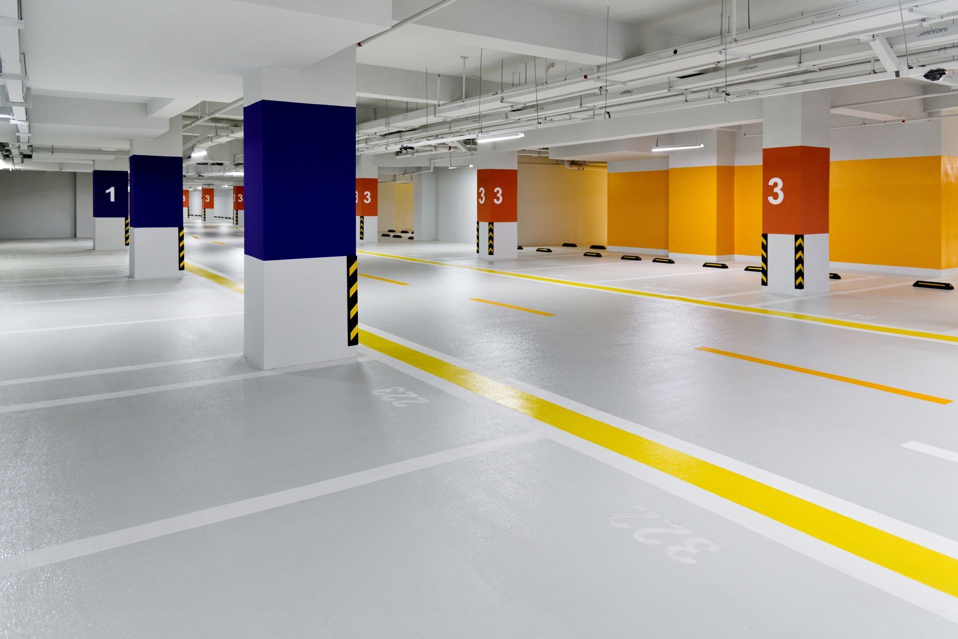 An empty parking garage with yellow lines and blue and orange pillars.