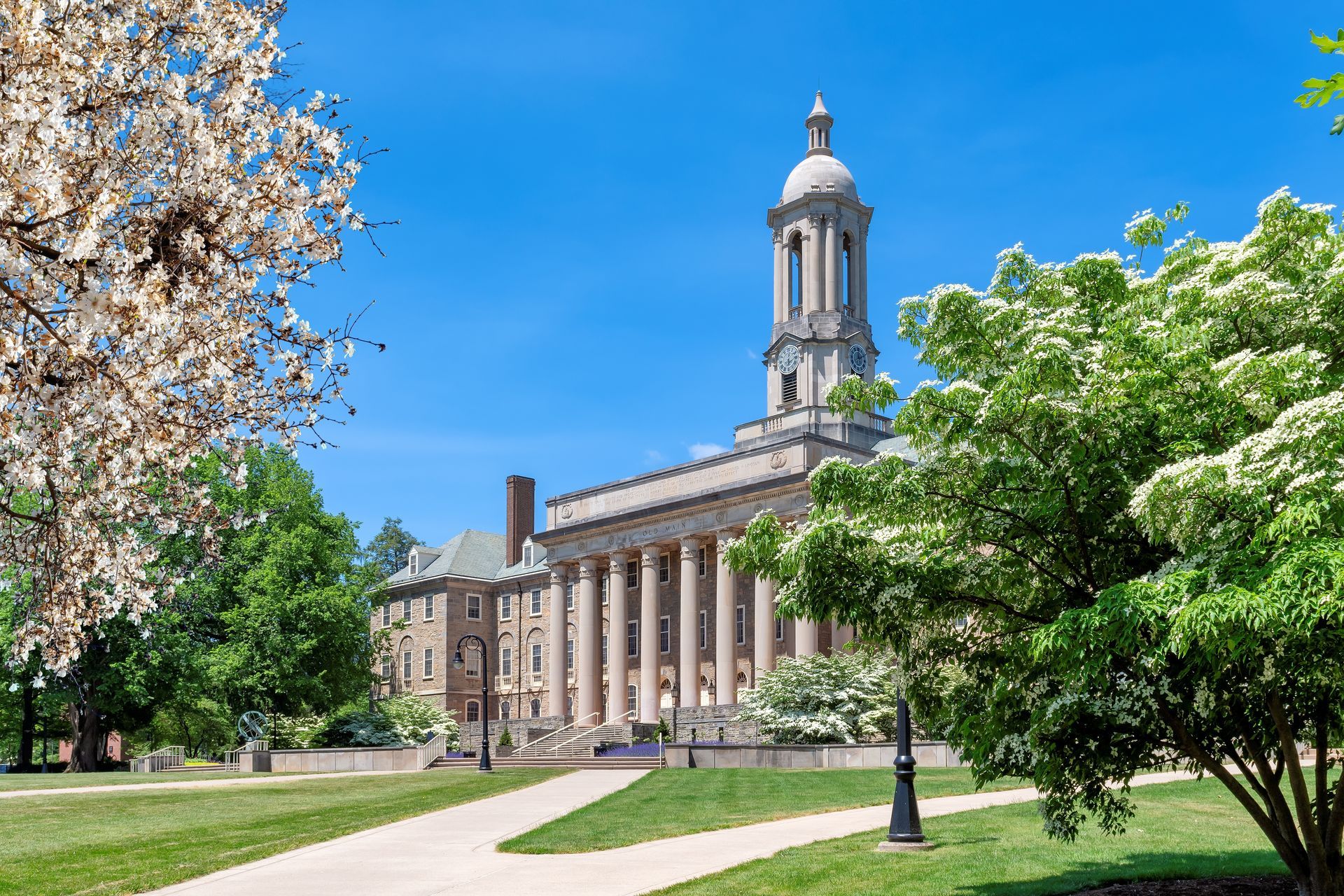 A large building with columns is surrounded by trees and grass on a sunny day.