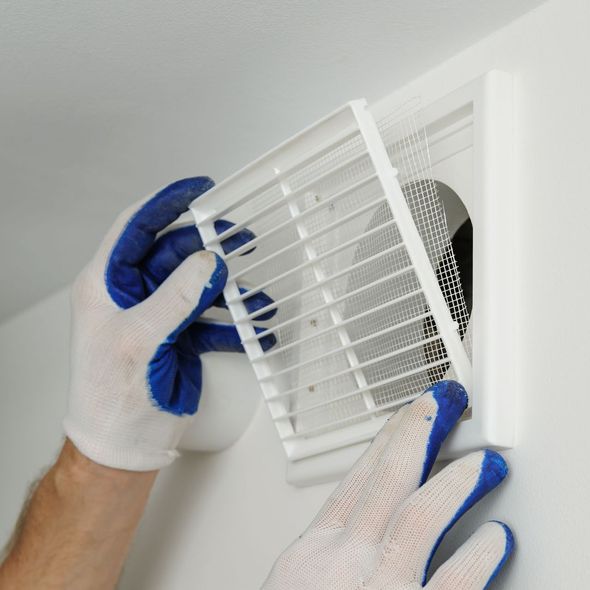 A person wearing blue gloves is fixing a vent on a wall