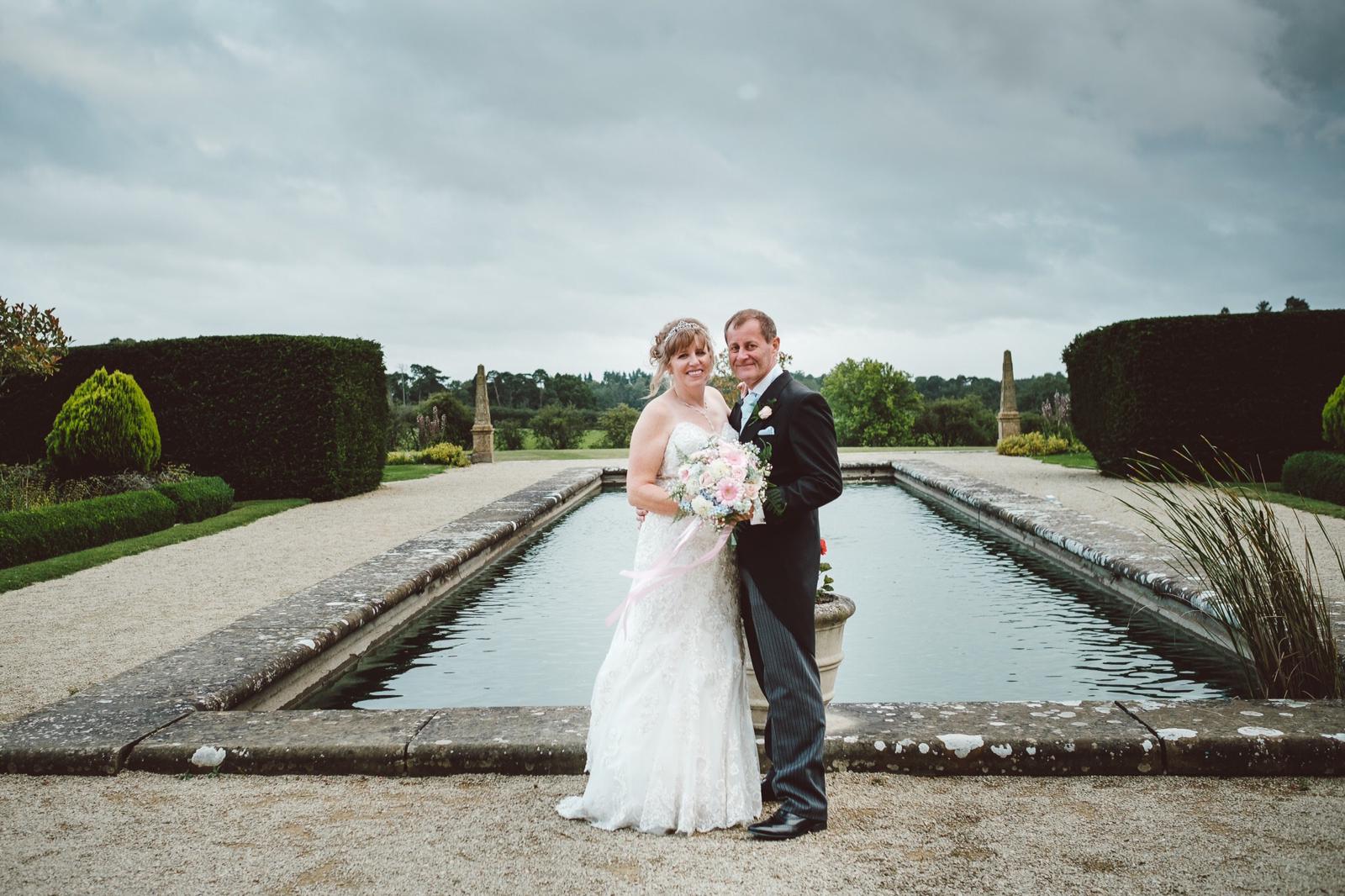 A bride and groom are posing for a picture in front of a pond.