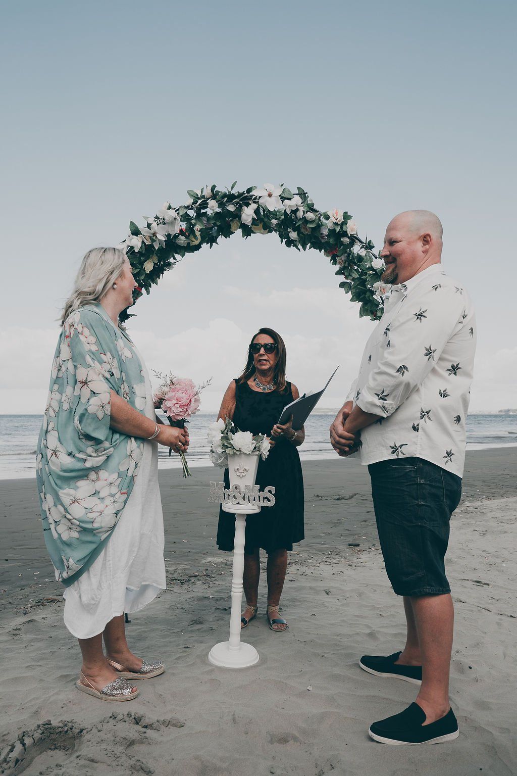 A man and a woman are standing on a beach during a wedding ceremony.