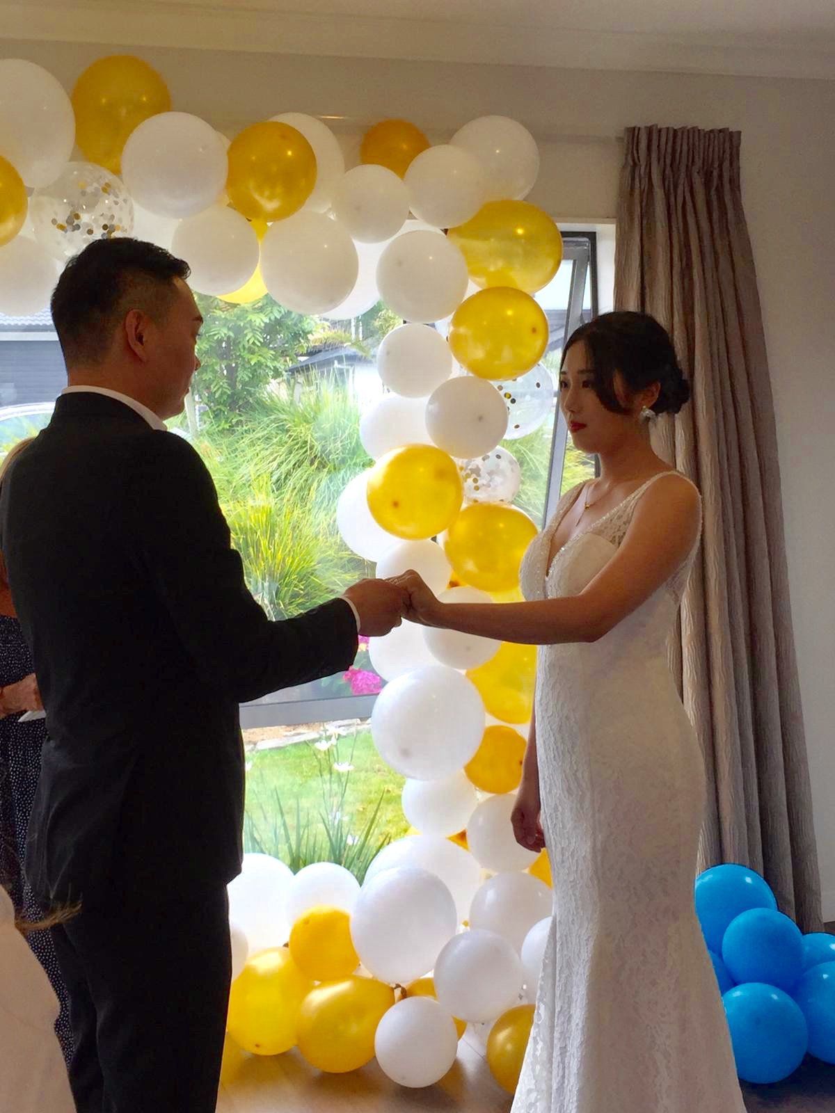 A bride and groom are holding hands in front of a balloon arch.
