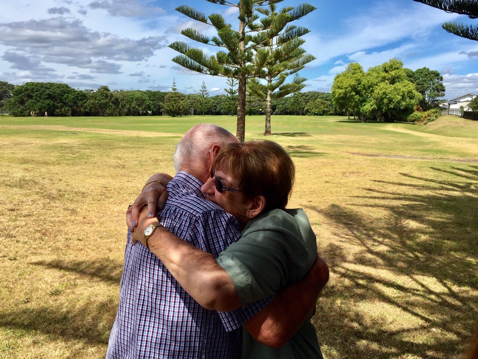 A woman is hugging an older man in a park.