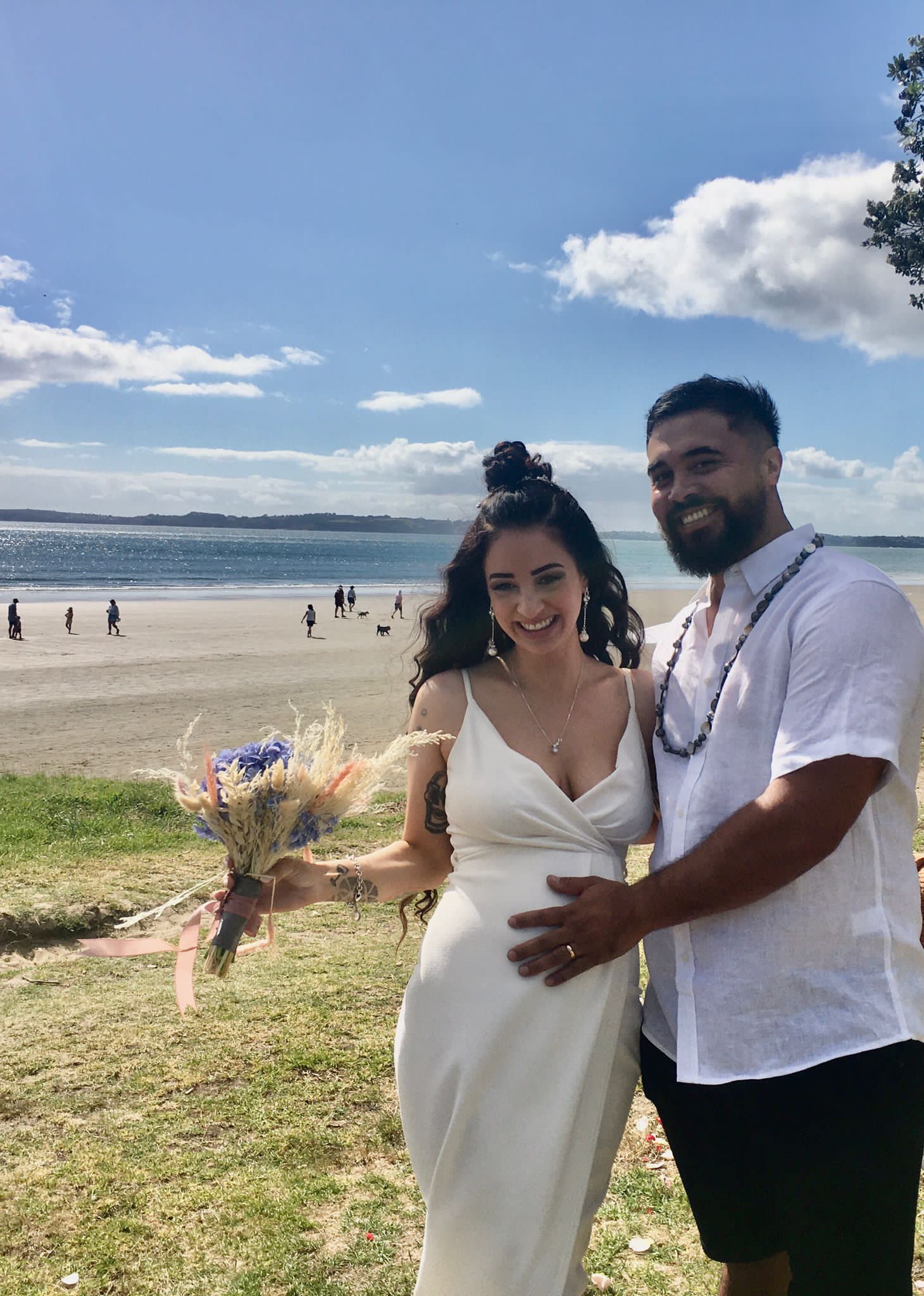 A bride and groom are posing for a picture on the beach.