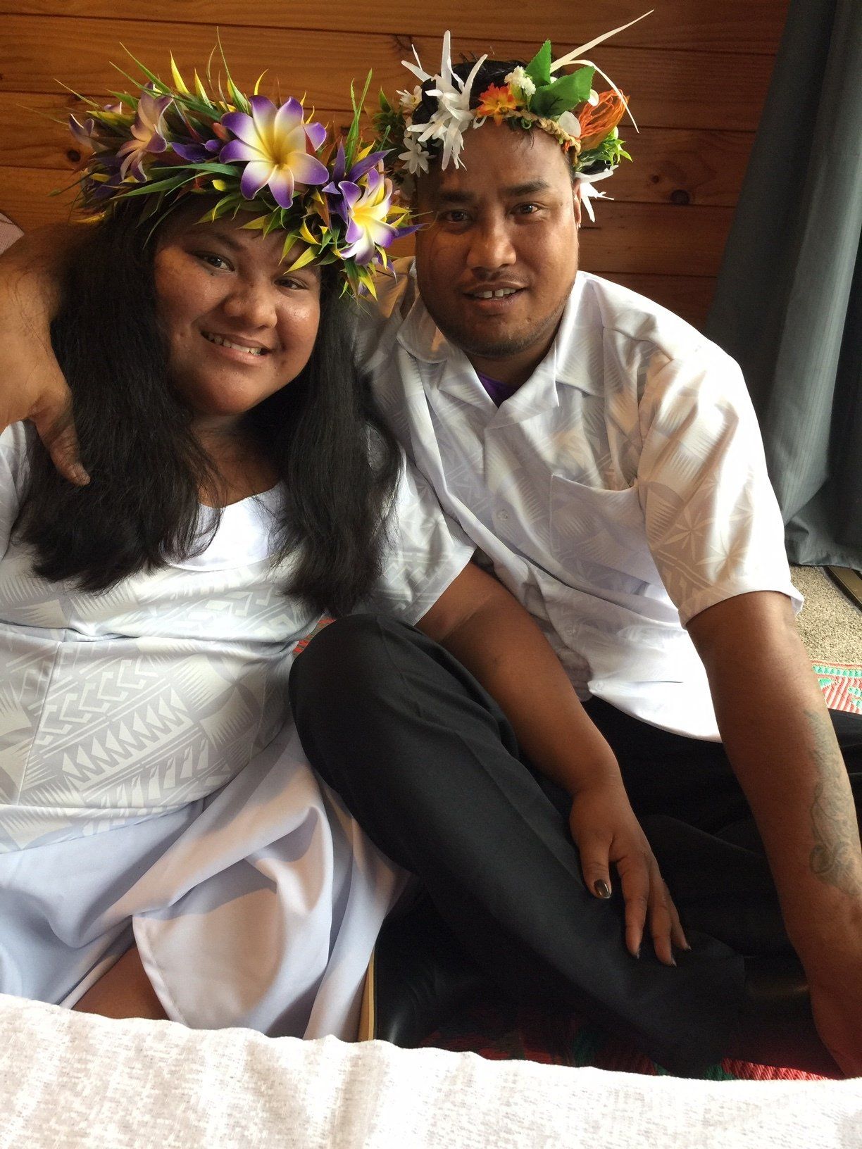 A man and a woman wearing flower crowns are sitting next to each other.